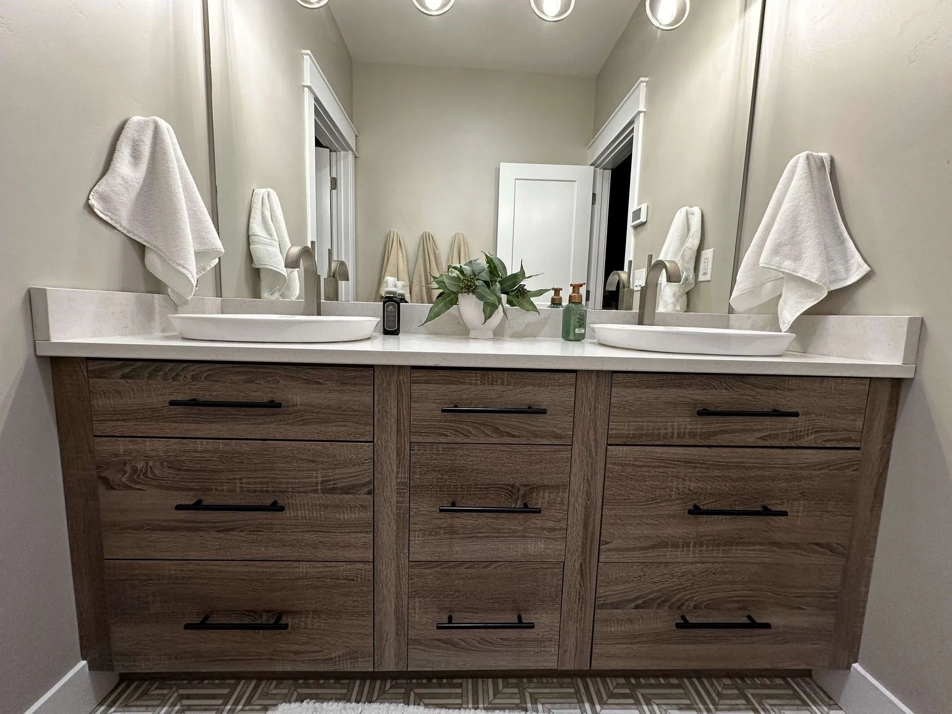 Bathroom vanity with two sinks, wood cabinets, and two mirrors with white towels.