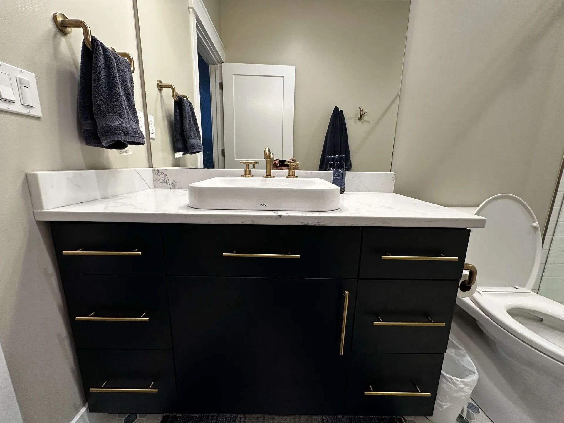 Bathroom with black vanity, white countertop, gold hardware, and a toilet.