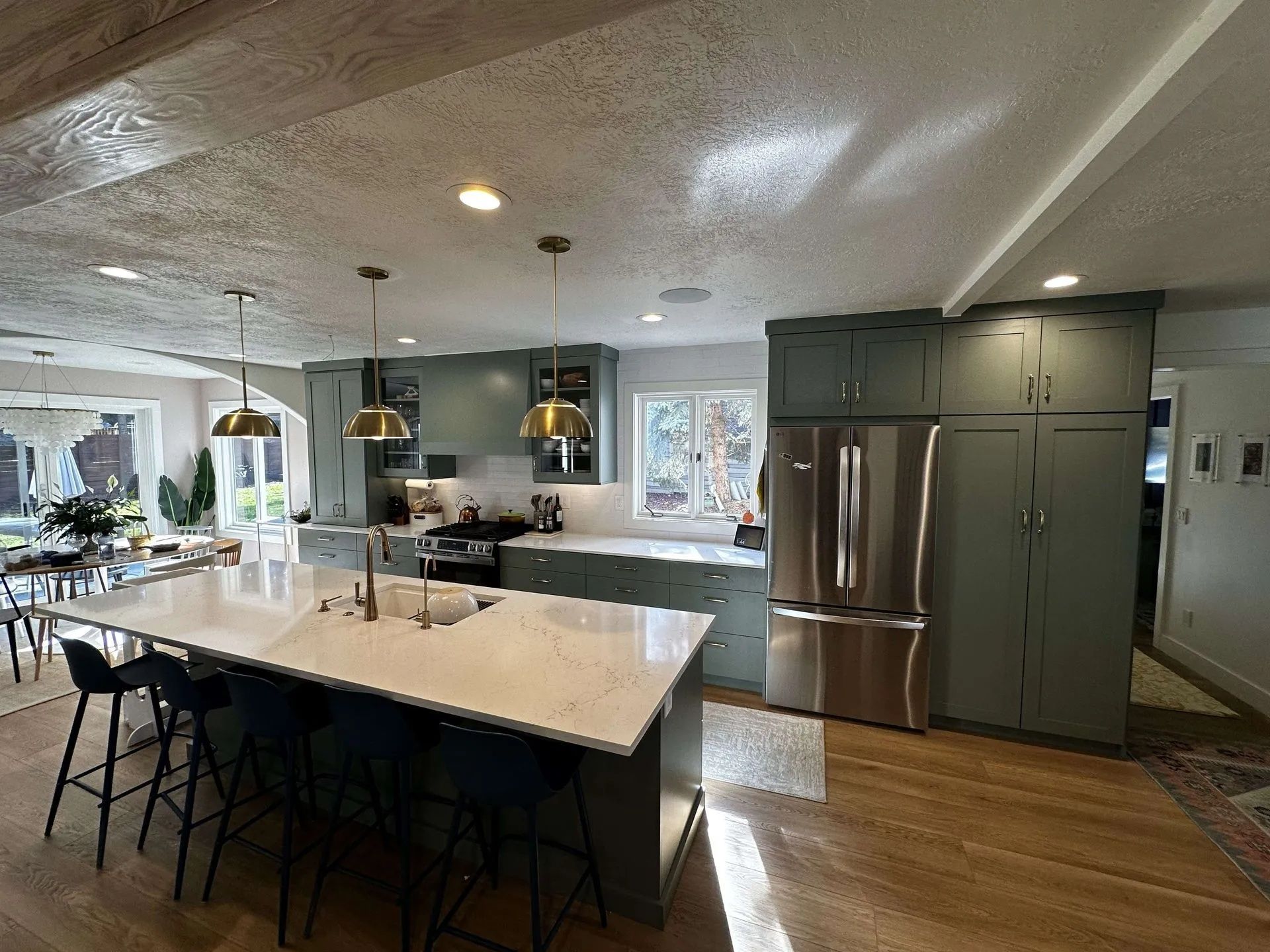 Spacious kitchen with a large island, green cabinets, stainless steel refrigerator, and pendant lights.