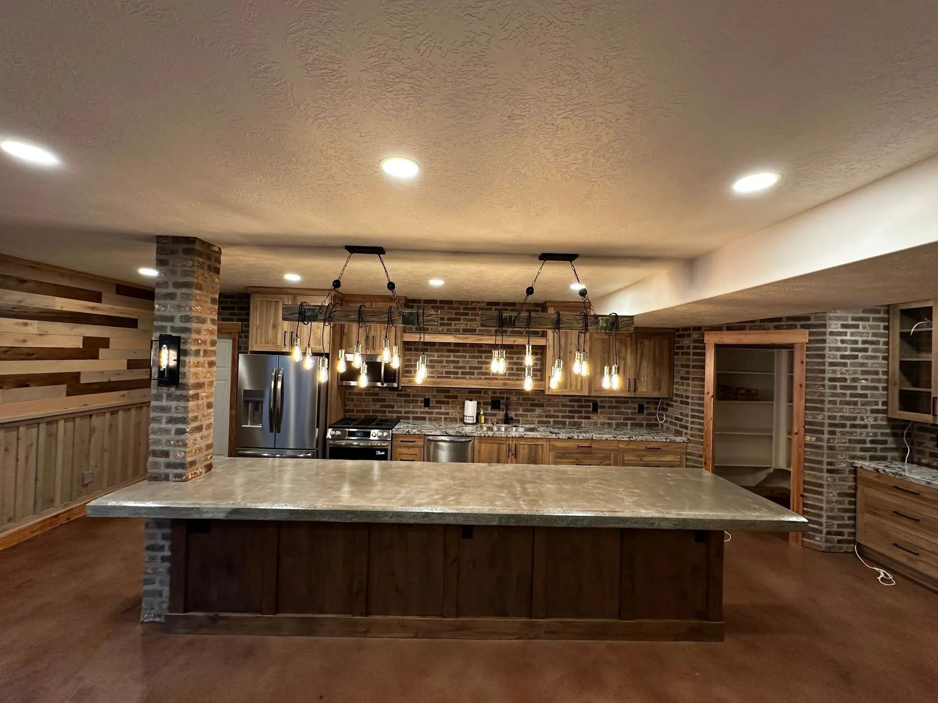 Rustic kitchen with wooden cabinets, brick accents, and a large island with overhead lighting.