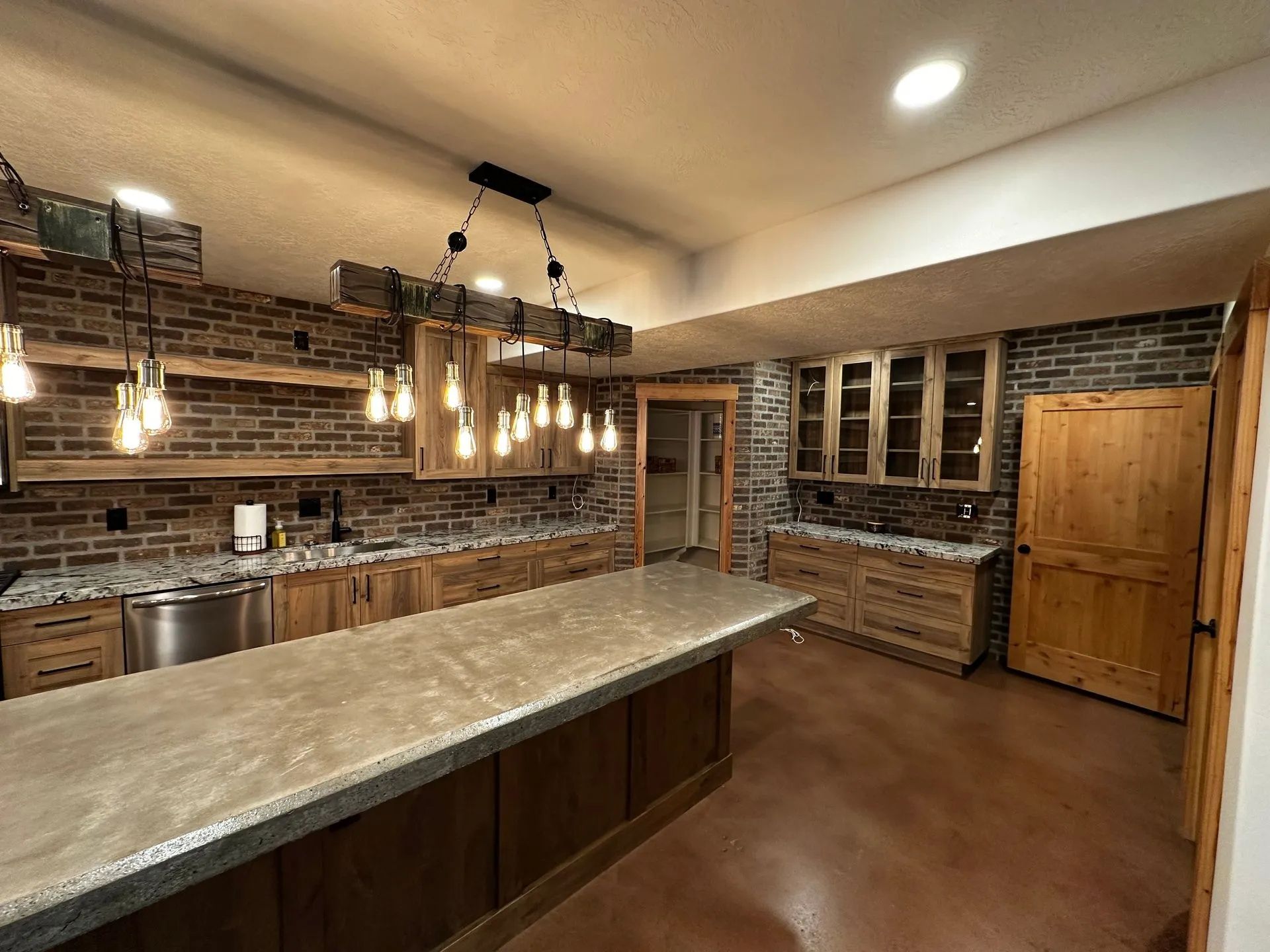 Rustic kitchen with brick backsplash, wood cabinets, island, and hanging light fixtures.