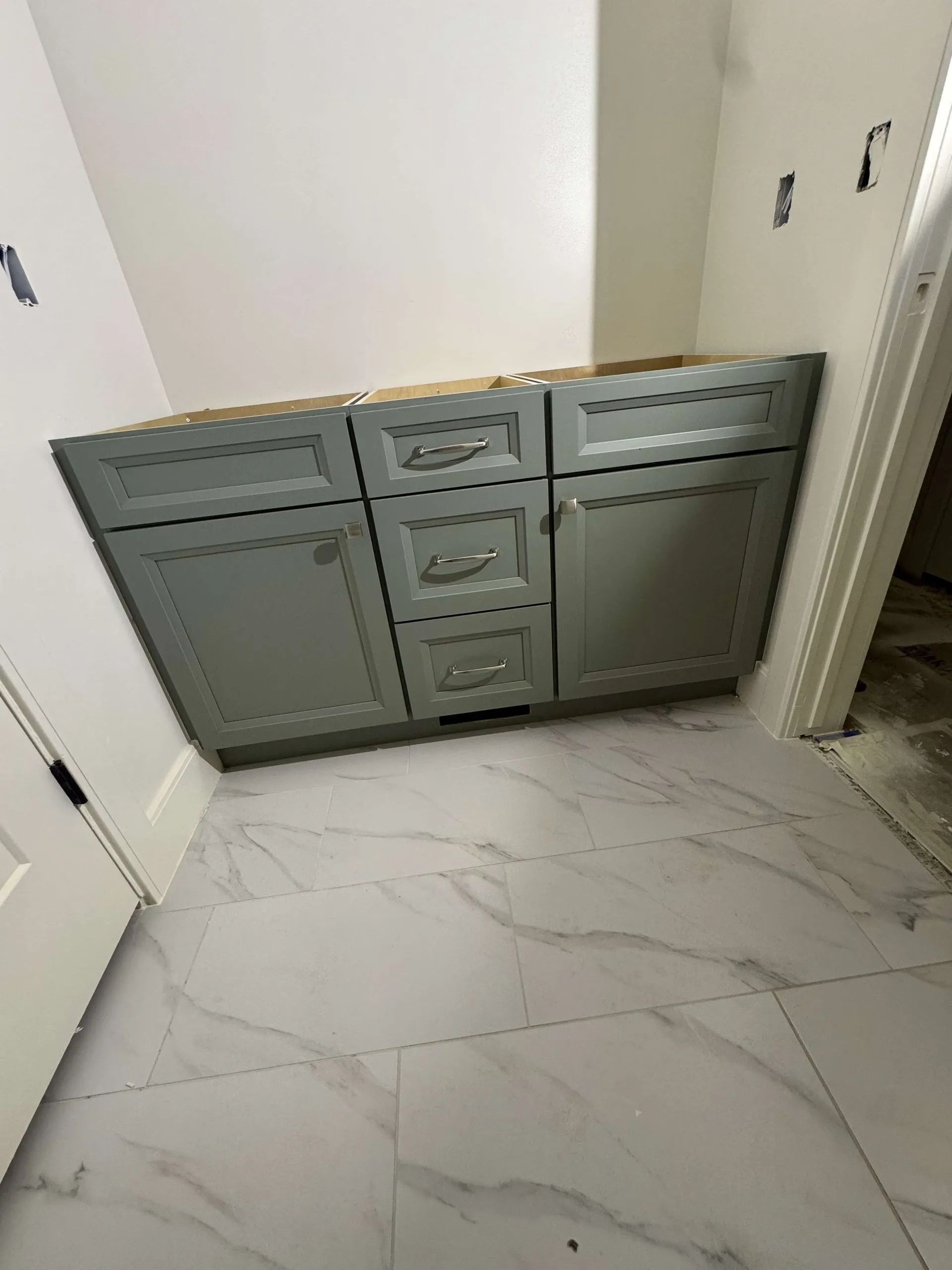 Gray bathroom cabinet on tiled floor, installed near a doorway, with bare walls.
