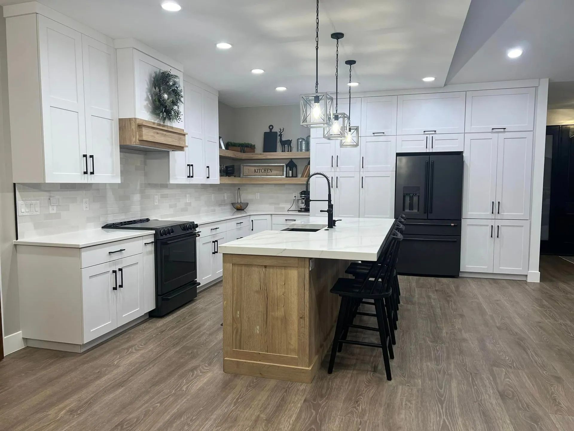 Modern white kitchen with black appliances, wood island, and pendant lights.