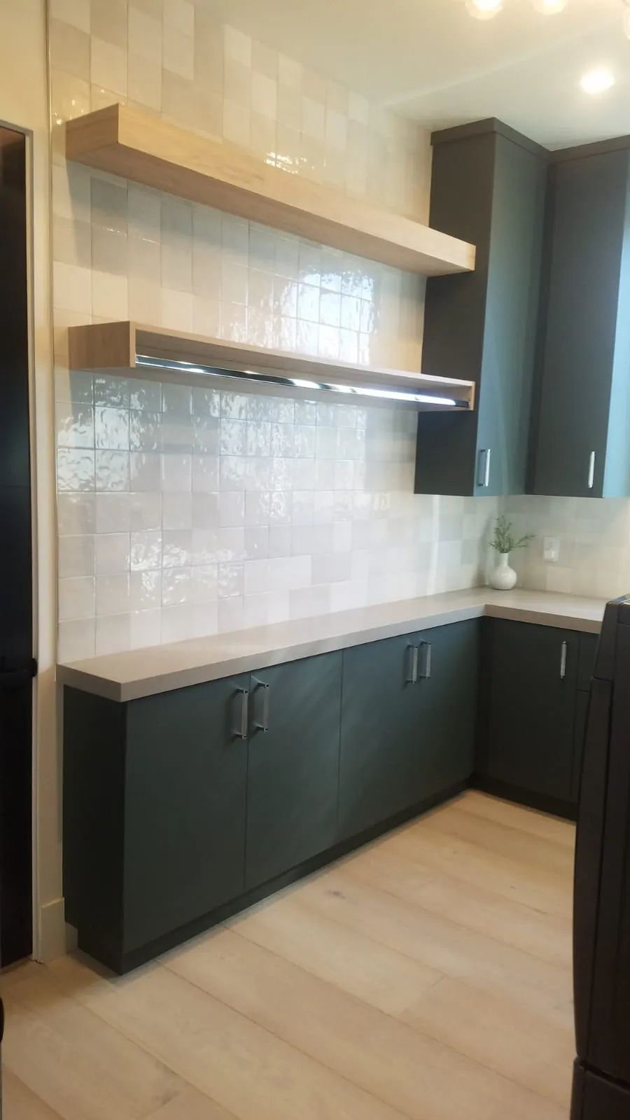 Kitchen with dark cabinets, light countertops, backsplash, and wooden shelves.