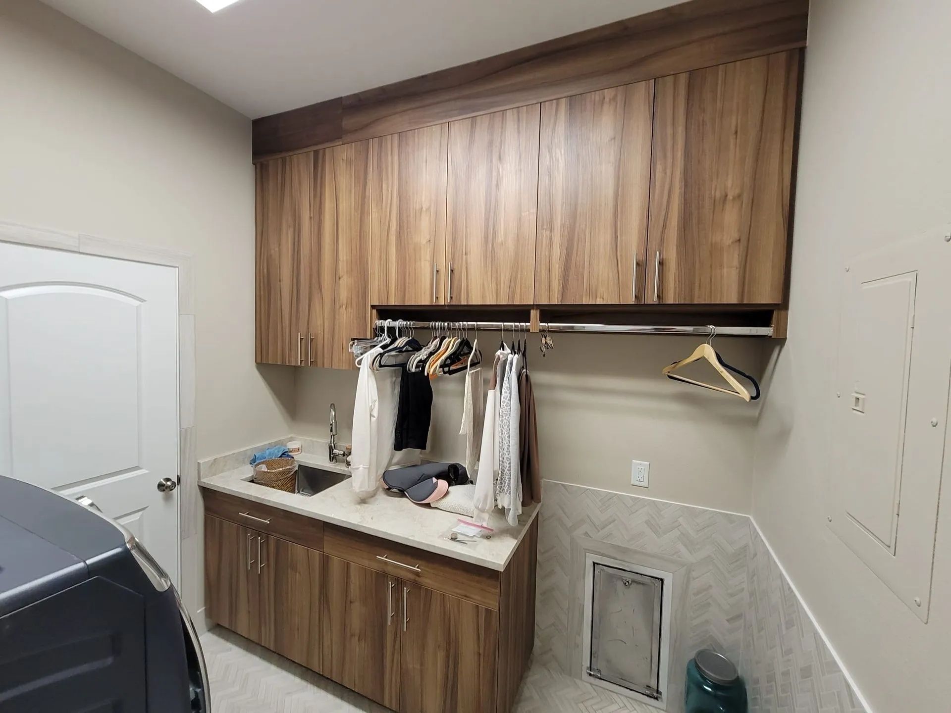 Laundry room with wooden cabinets, sink, drying rack, and hanging clothes.