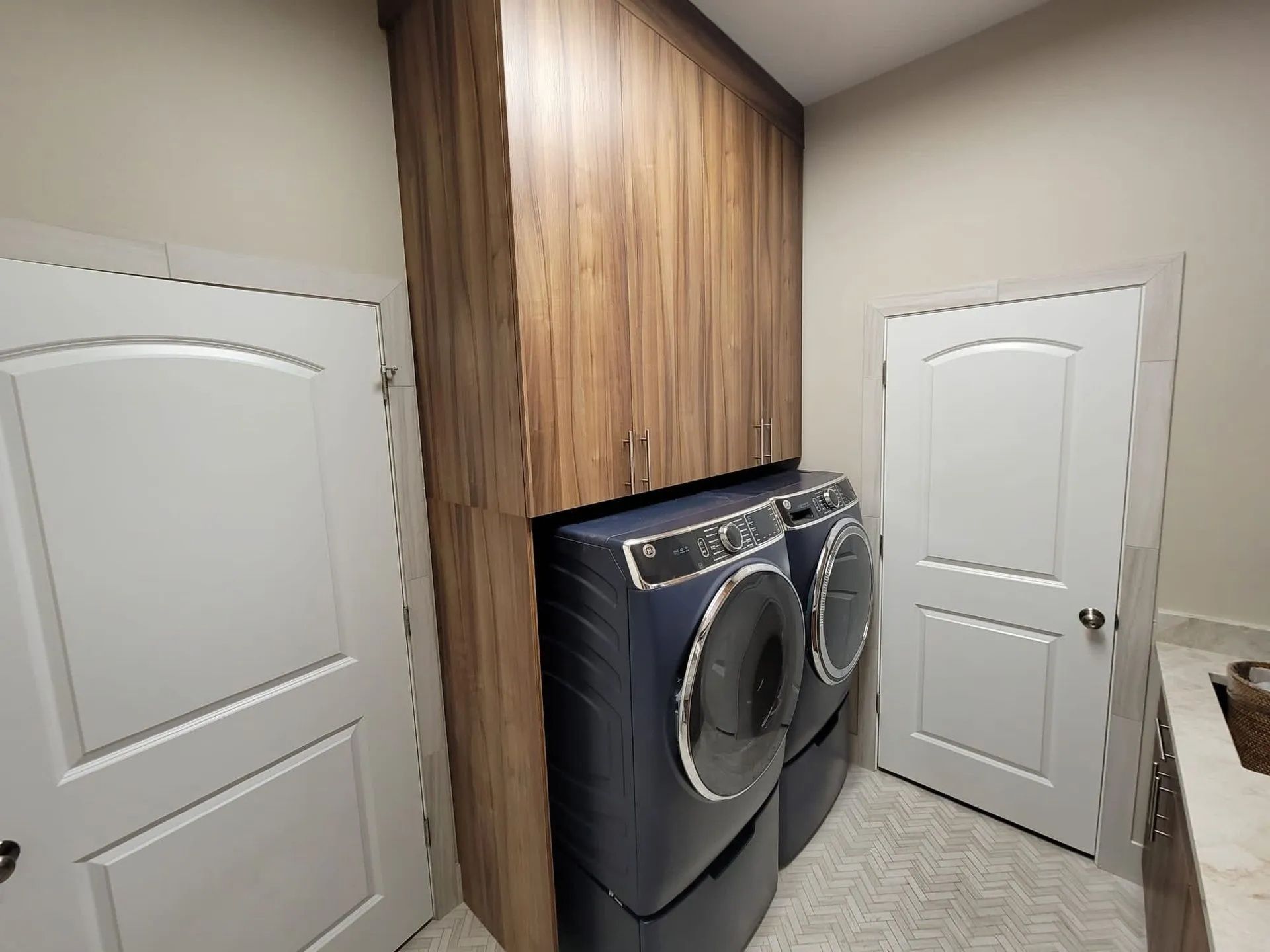Laundry room with wood-grain cabinets and blue washer/dryer. Two white doors flank the cabinets.