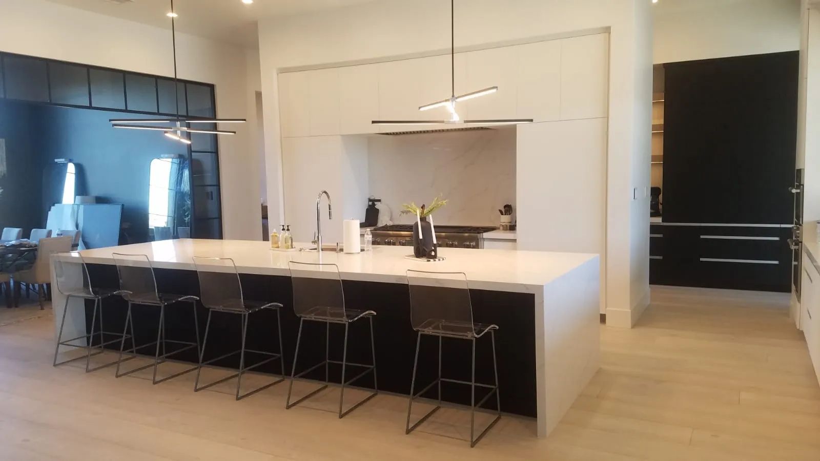 Modern kitchen with large white island, dark cabinets, and several barstools.