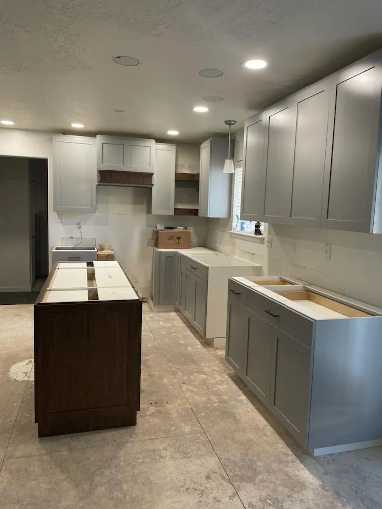 Kitchen remodel in progress: gray and brown cabinets, unfinished countertops, exposed walls, and concrete floors.