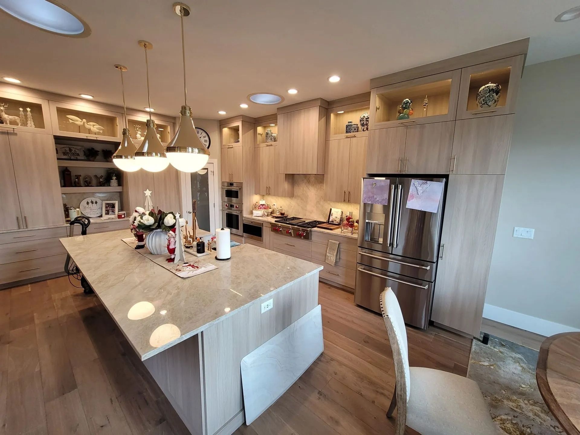 A bright, modern kitchen with light wood cabinets, an island, and stainless steel appliances.
