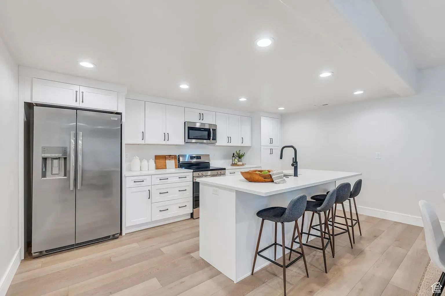 Modern kitchen with white cabinets, stainless steel appliances, and a kitchen island with bar stools.