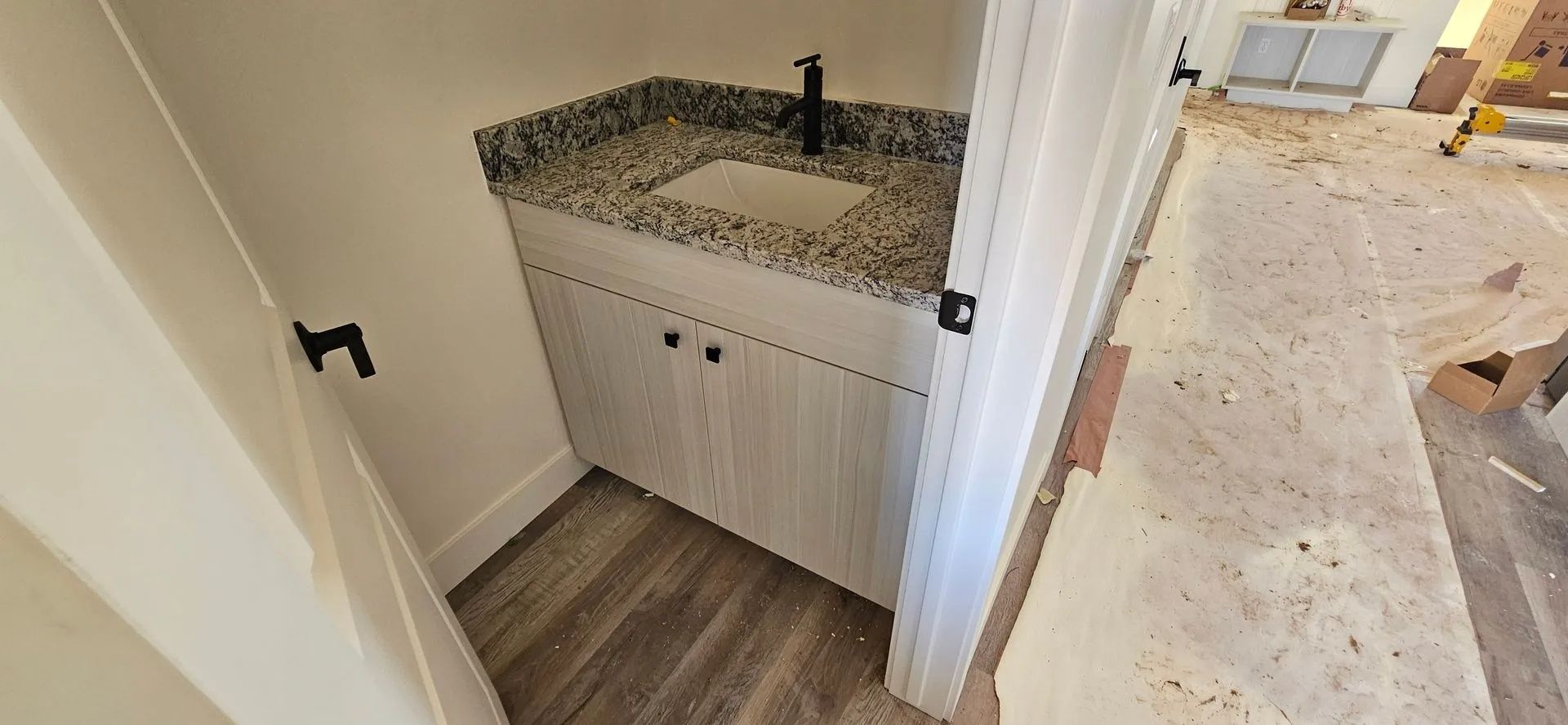 A small bathroom with a white cabinet, granite countertop sink, and a black faucet.