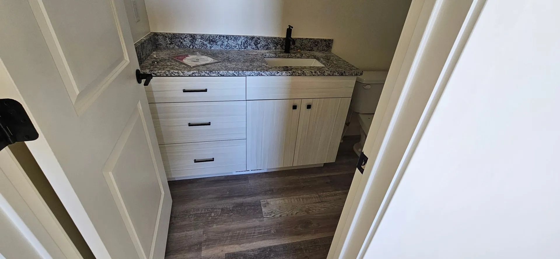 Bathroom with white vanity, gray countertop, and dark faucet. Doorway in view.