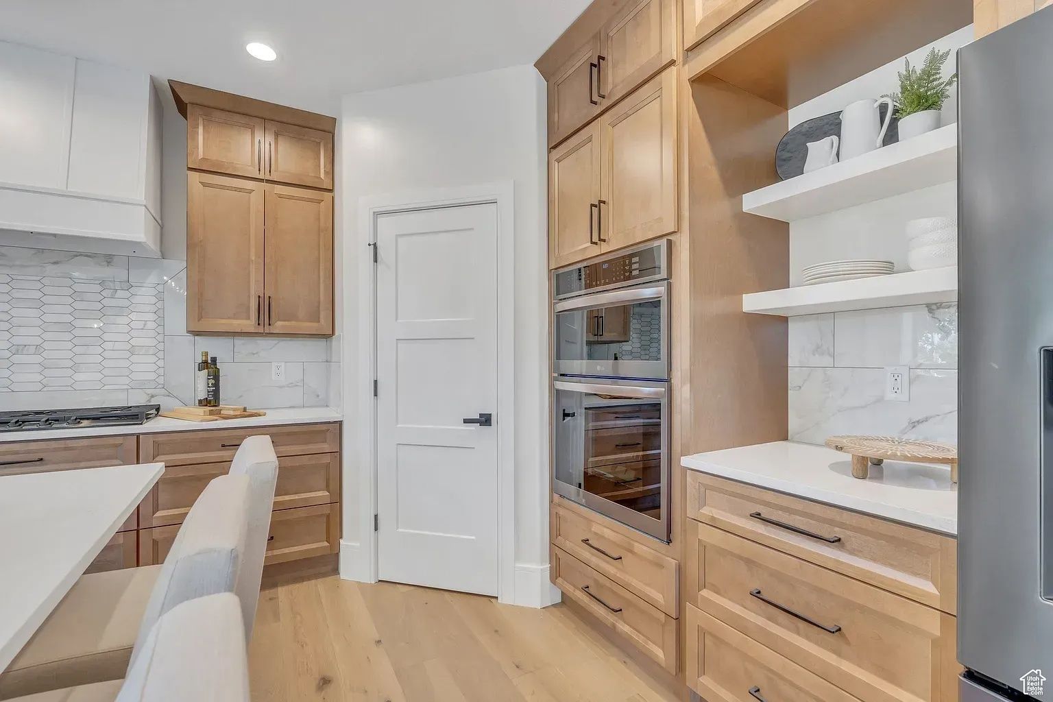 Kitchen with wood cabinets, white countertops, double ovens, and open shelves.