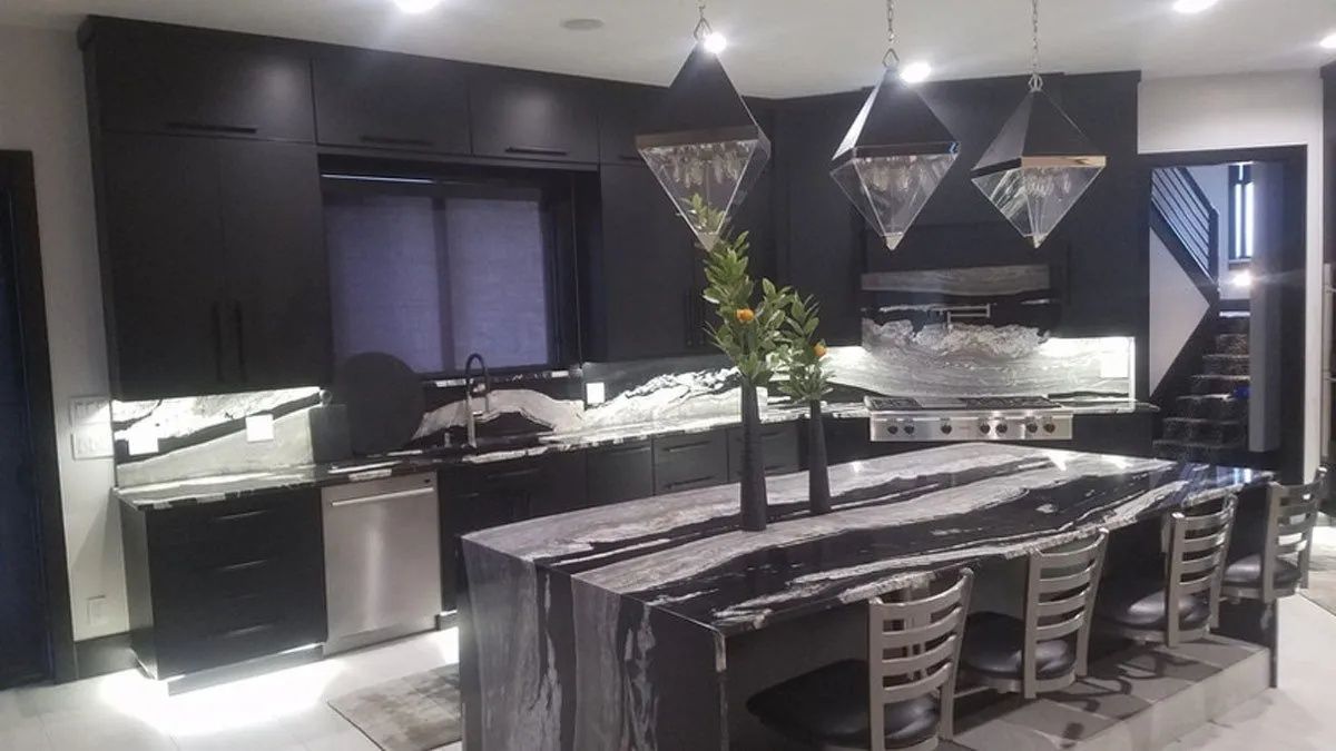 Modern black kitchen with a large island with gray countertops and three decorative hanging lights.