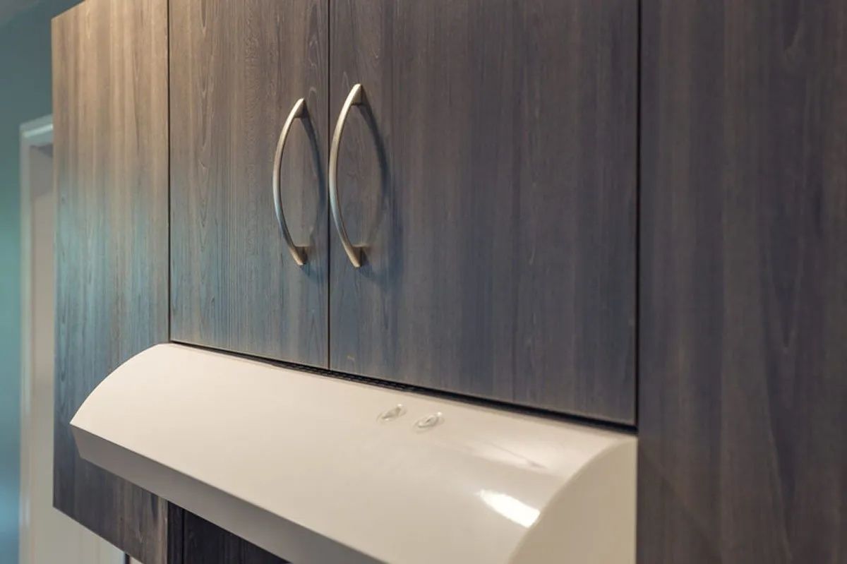 Kitchen cabinets above a white range hood, with silver handles on the gray-blue cabinets.