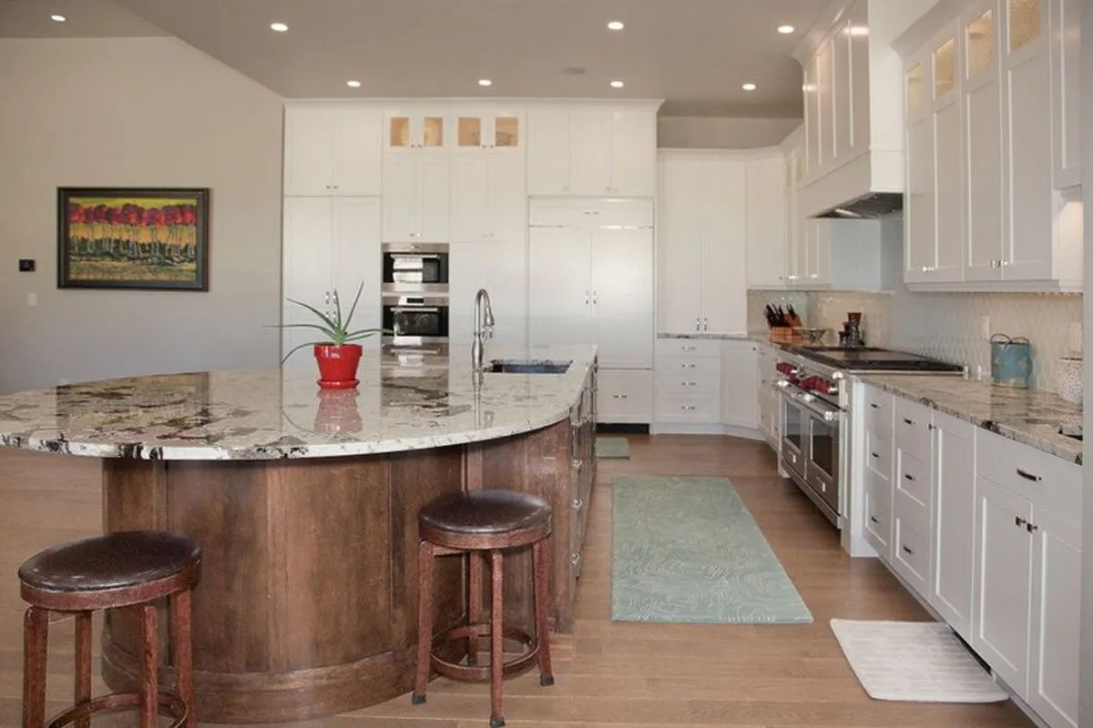 Spacious white kitchen with dark wood island, granite countertops, stainless steel appliances, and two brown stools.
