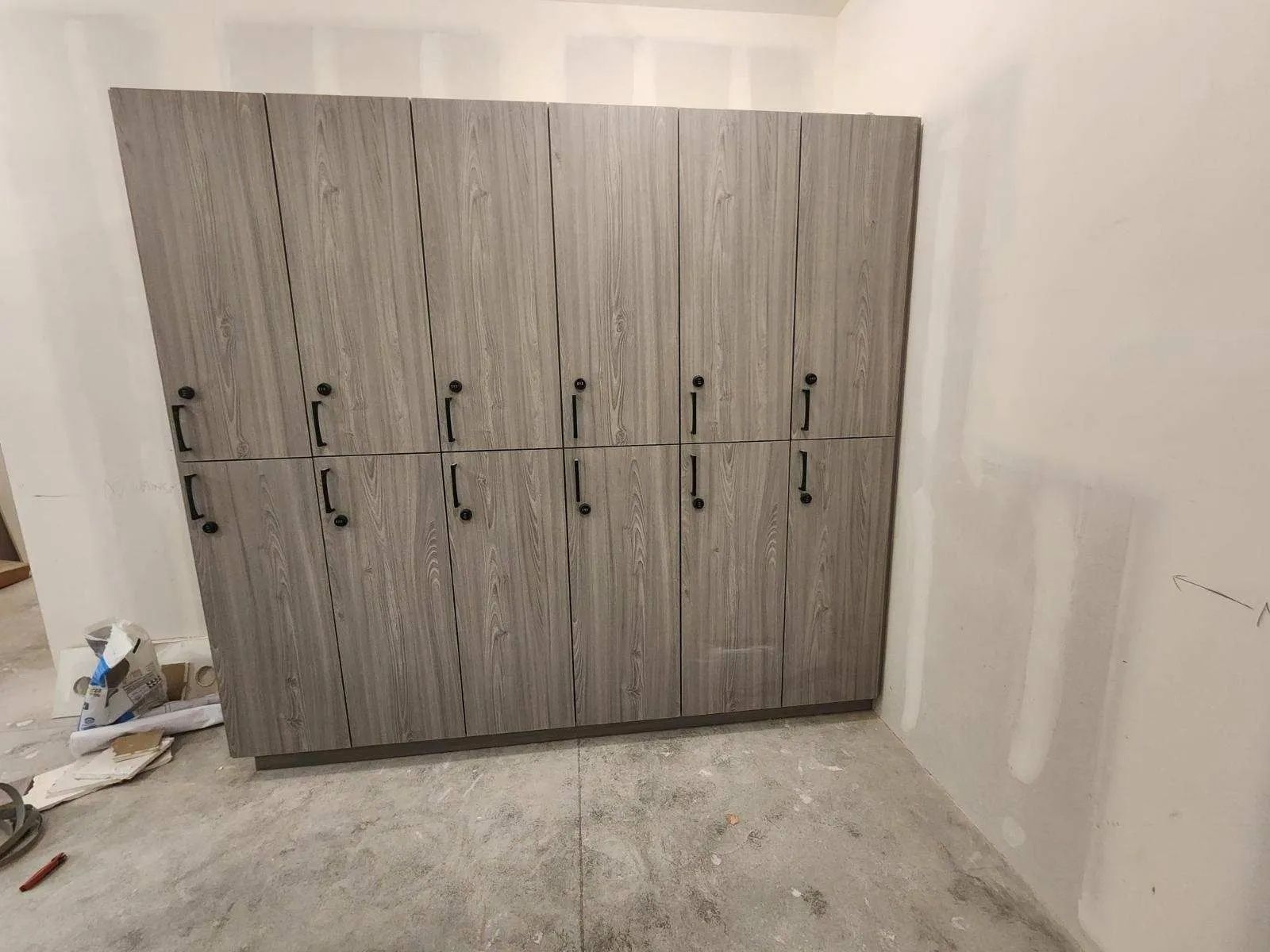 Tall gray storage cabinets with black handles in a room with unfinished walls and flooring.