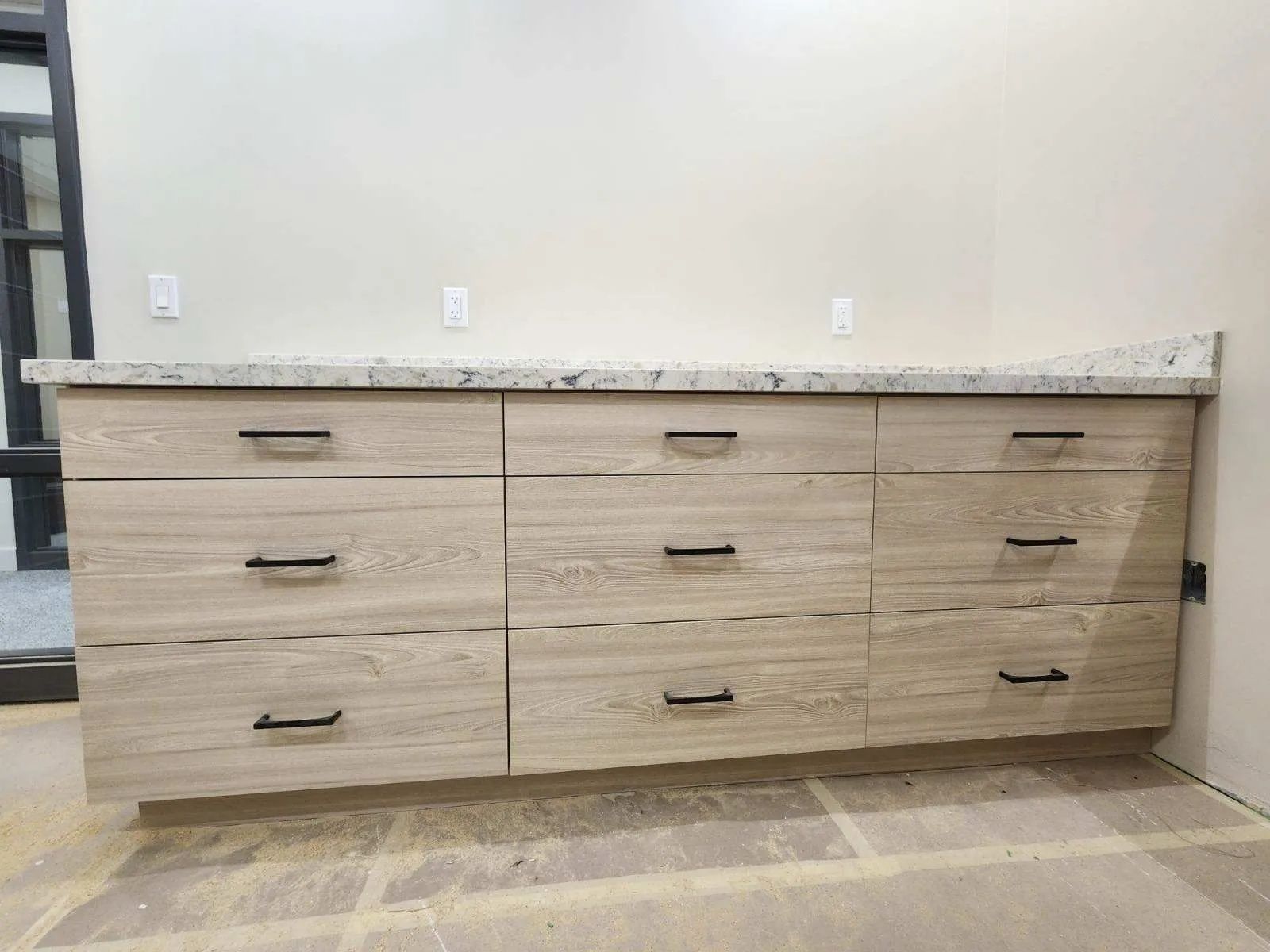 Light wood cabinets with black handles, set under a light granite countertop against a beige wall.