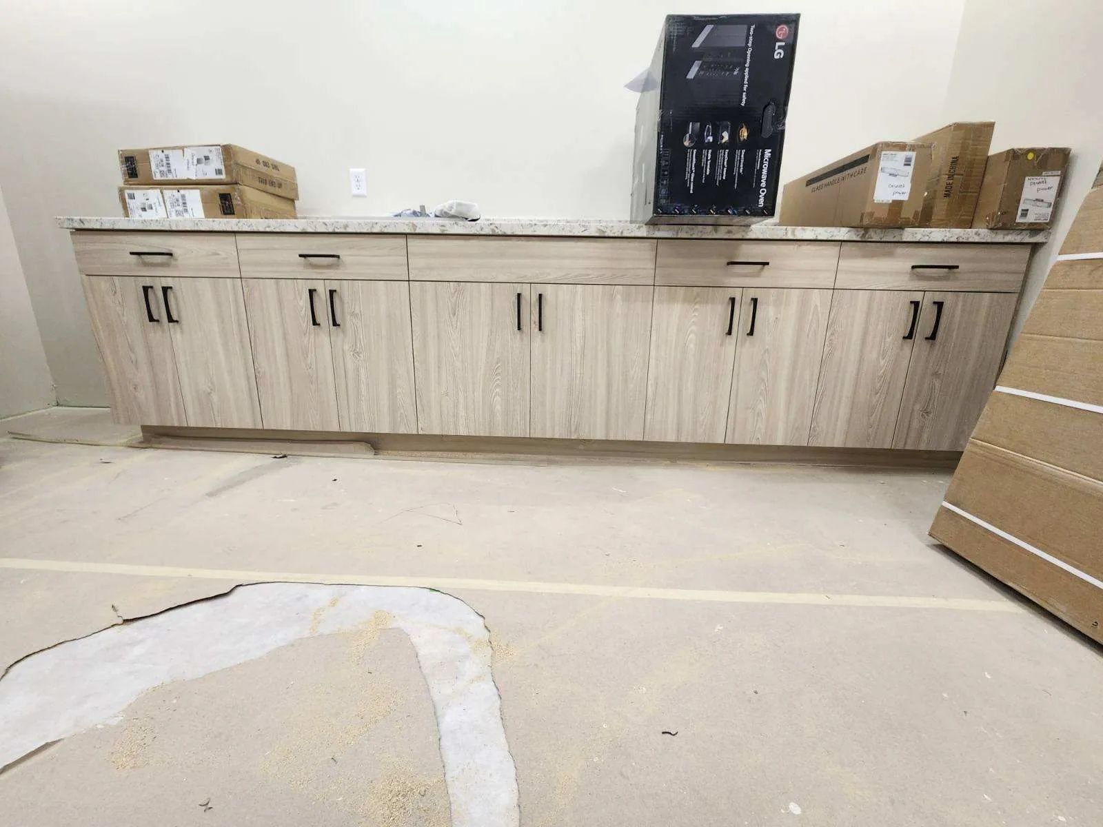 Long cabinets with light wood doors and granite countertop against a white wall; boxes and a tower computer are on the countertop.