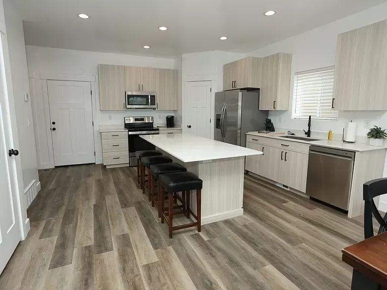 Modern kitchen with light wood cabinets, stainless steel appliances, white countertops, and a large island with bar stools.