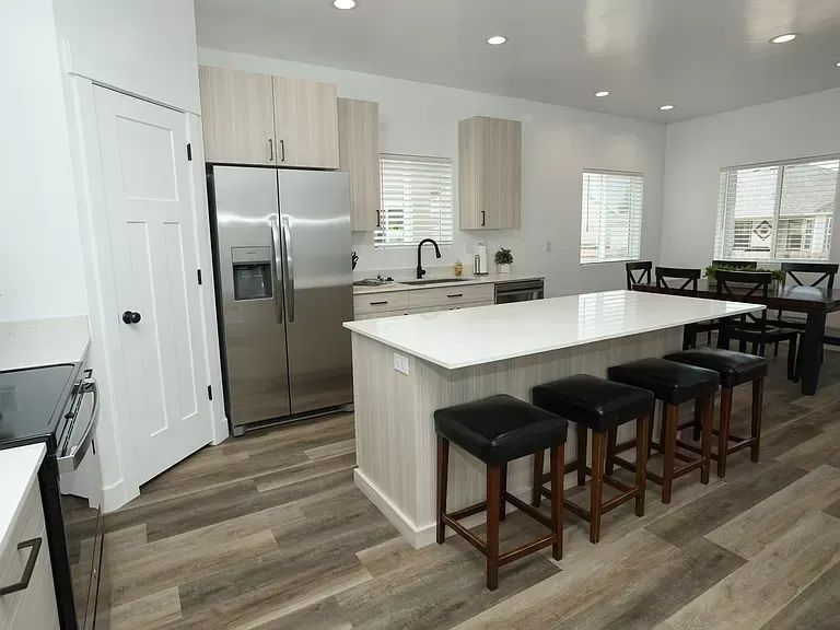 Modern kitchen with stainless steel appliances, island with stools, and dining table.