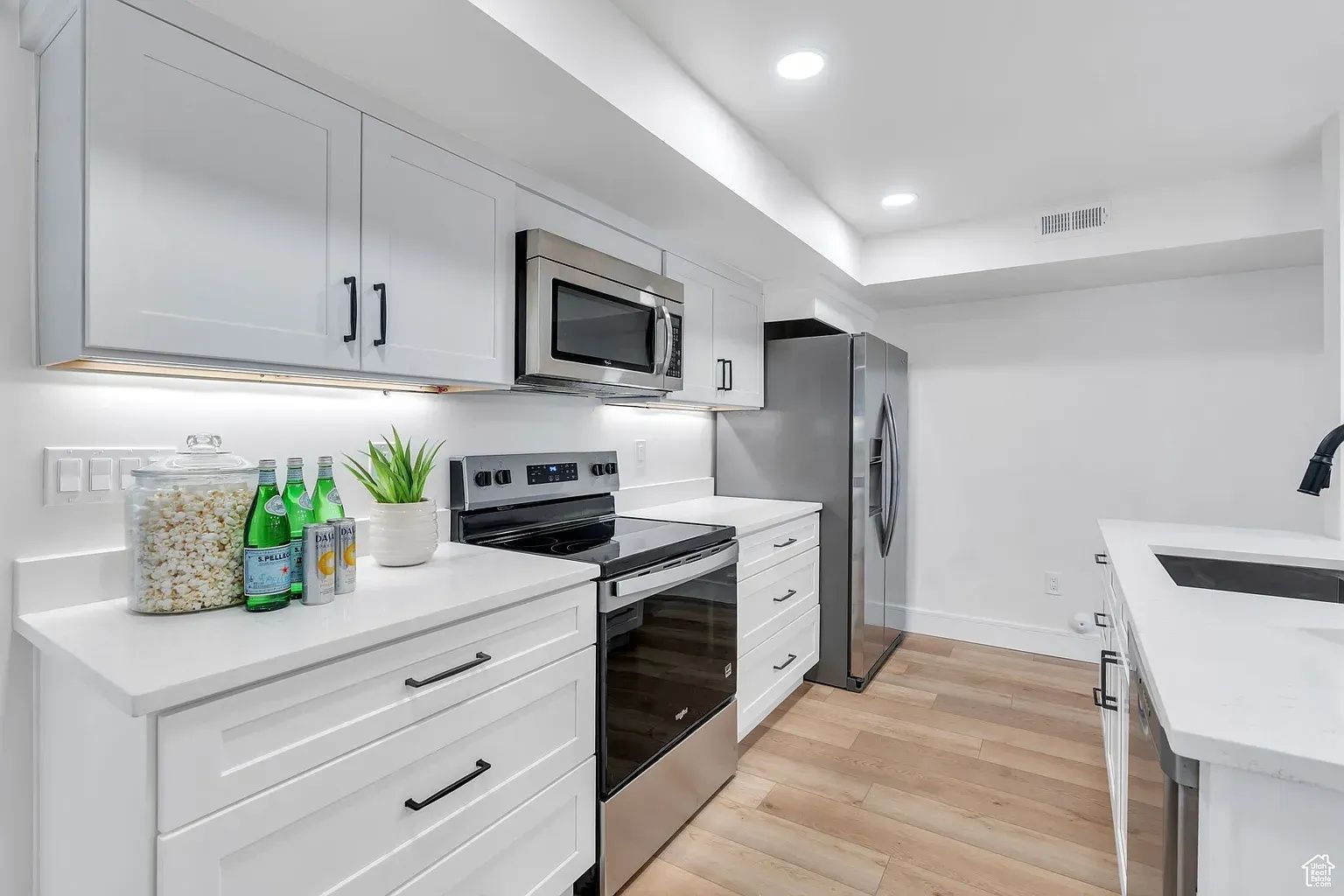 Modern white kitchen with stainless steel appliances, white cabinets, and light wood flooring.