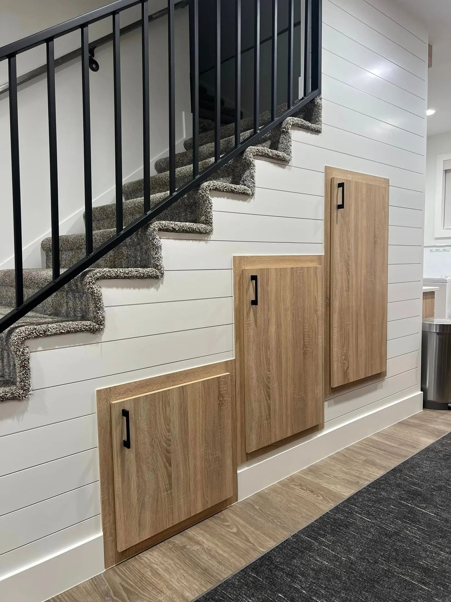 Staircase with built-in wooden storage cabinets along the wall. Black railing and carpeted steps.