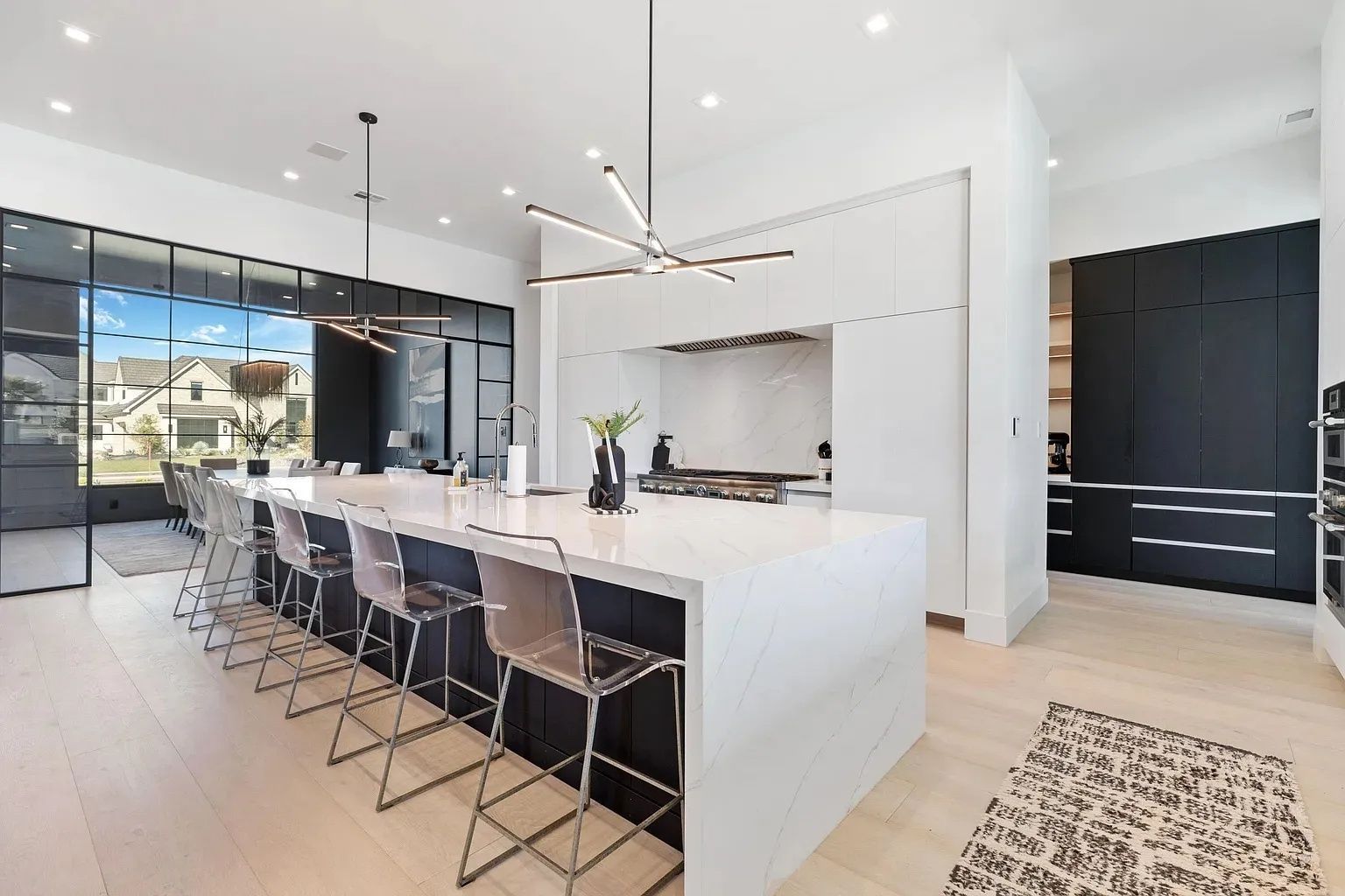 Modern kitchen with island, seating, and large windows. Black and white color scheme.