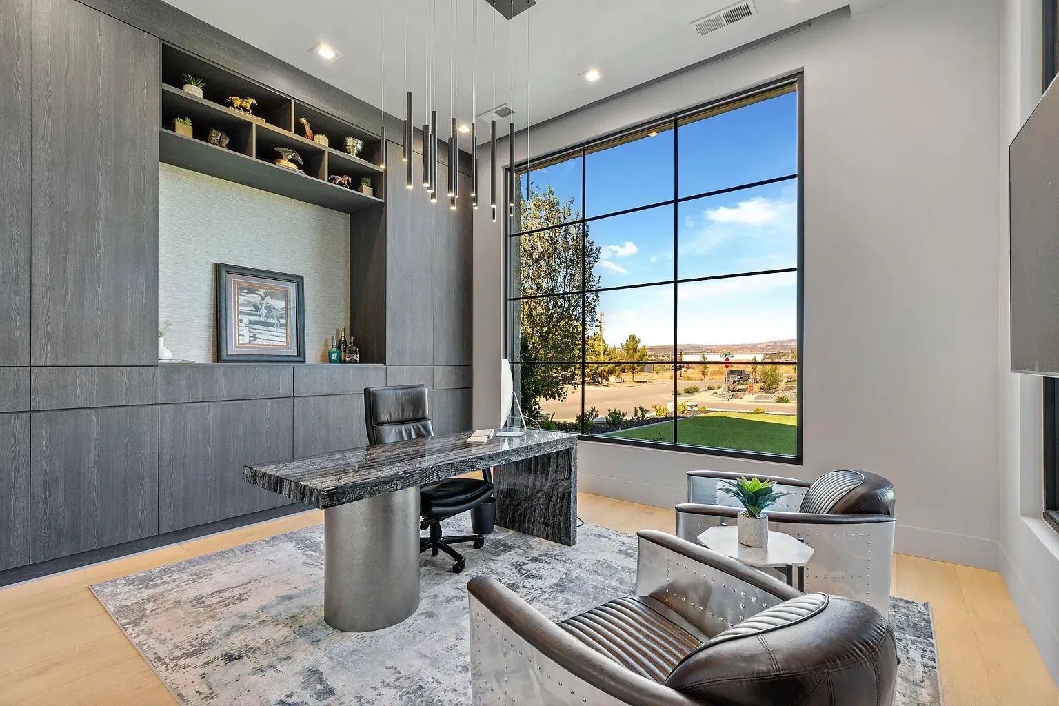 Modern office with large window overlooking a landscape. Includes desk, chairs, shelving, and a decorative light fixture.