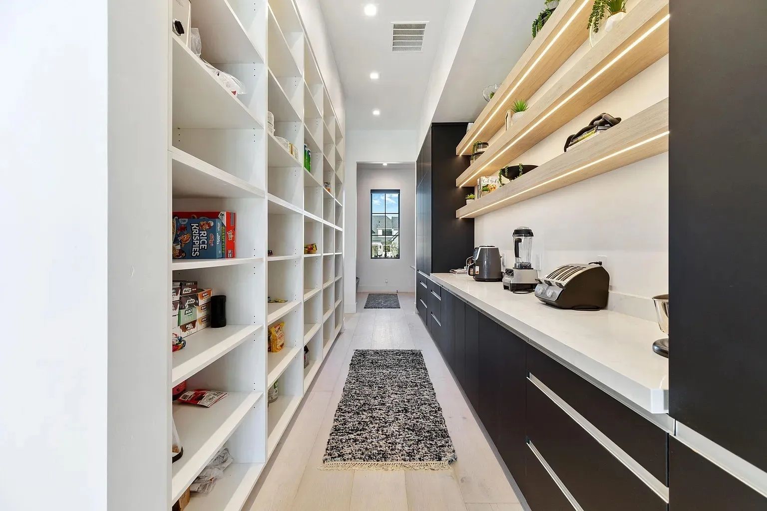 Pantry with floor-to-ceiling shelves on left, countertop and shelves on right, rug on floor, door at end.