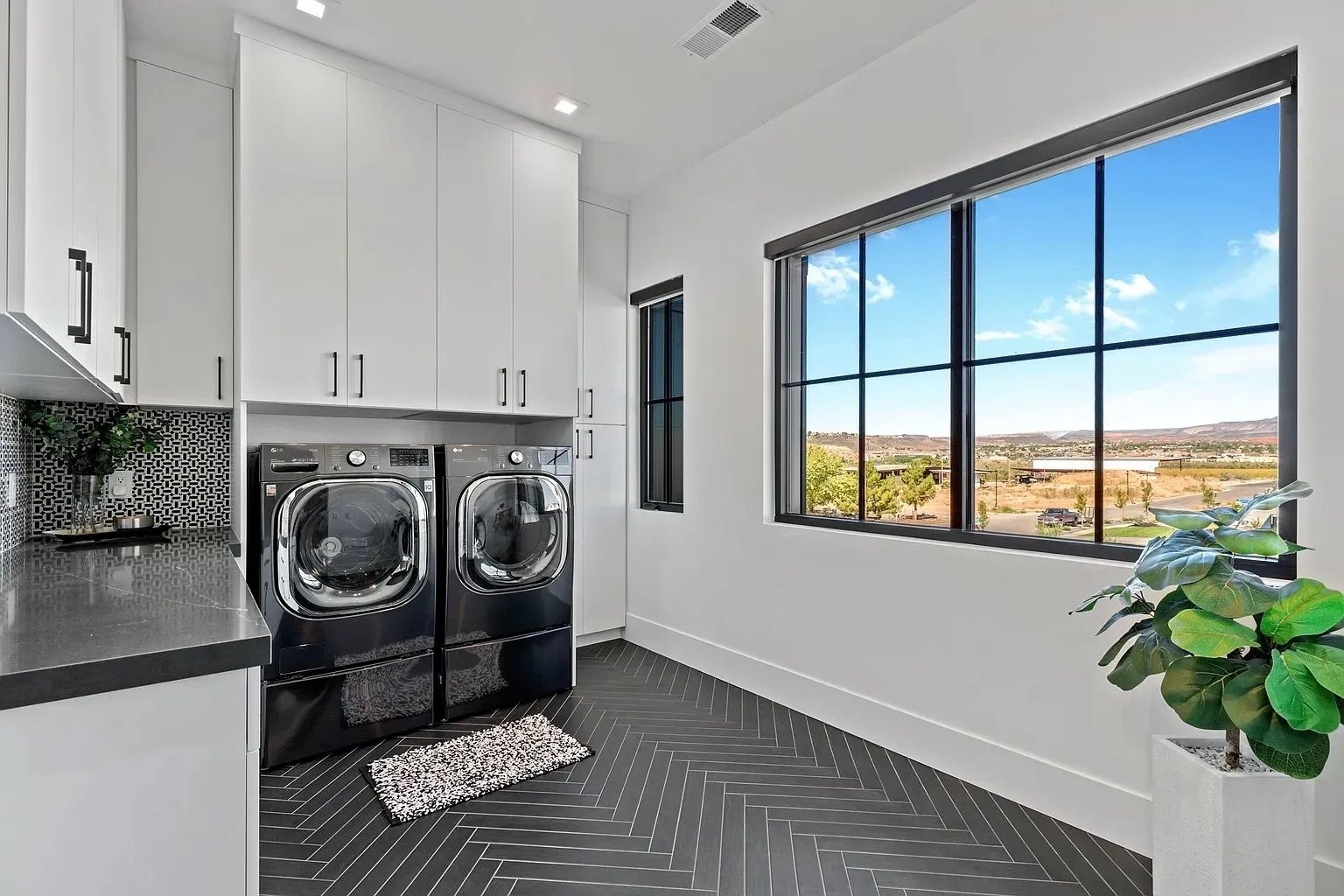 Laundry room with black appliances, white cabinets, patterned floor, and large window with a view.