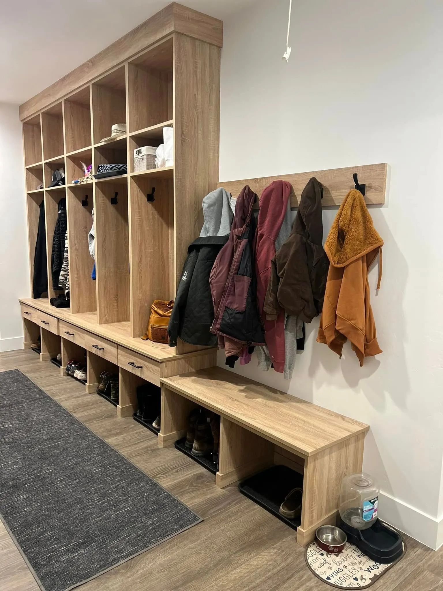 Wooden entryway with cubbies, shoe storage, bench, and coat rack; rug on floor.