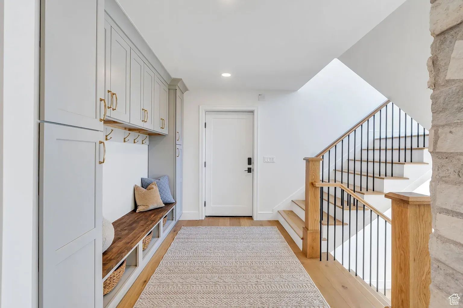 Hallway with built-in storage bench, door, and staircase with wood and black metal railing.