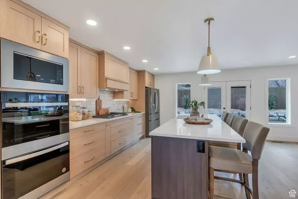 Modern kitchen with light wood cabinets, stainless steel appliances, and island with bar seating.