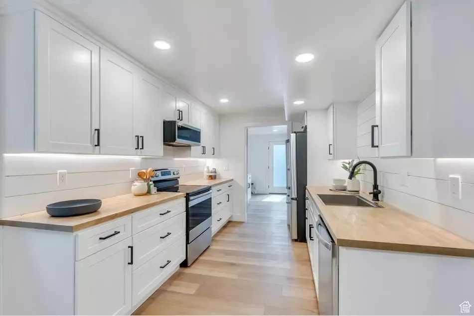 Bright, narrow kitchen with white cabinets, wood countertops, and stainless steel appliances.