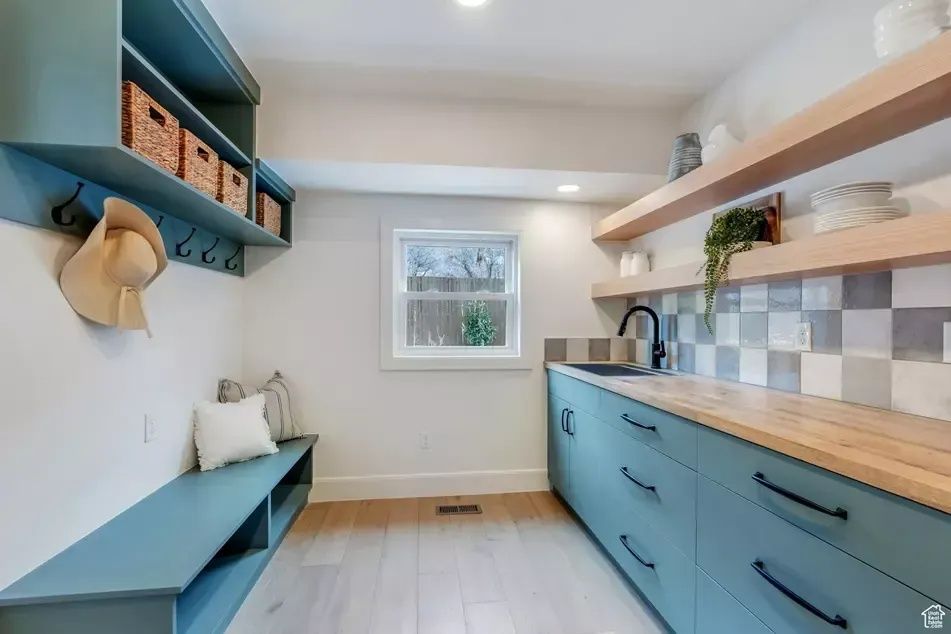Laundry room with blue cabinets, wooden shelves, a bench, and a small window.