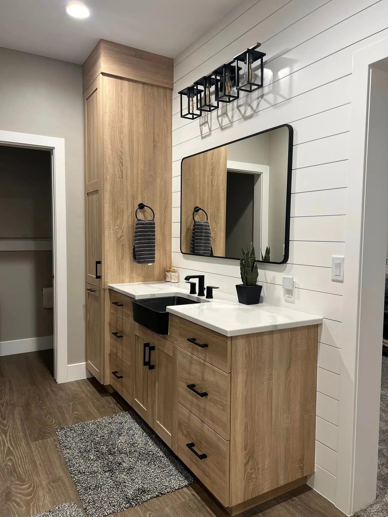 Bathroom with wood cabinets, black fixtures, white countertop, shiplap wall, and black-framed mirror.