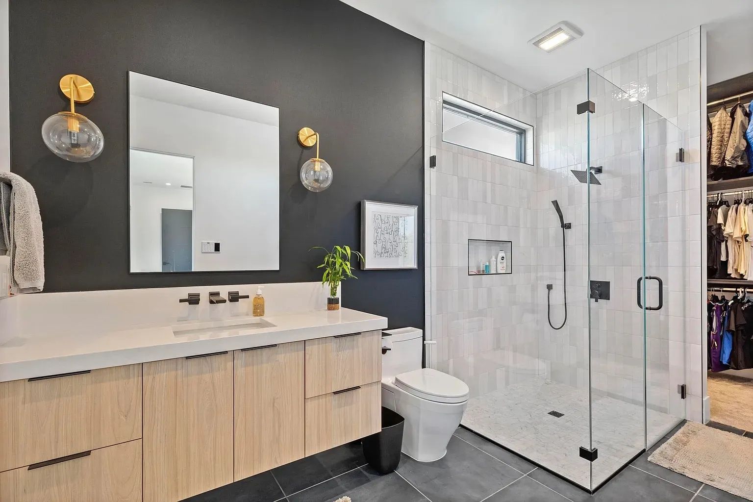 Modern bathroom with wood vanity, black accent wall, glass shower, and walk-in closet.