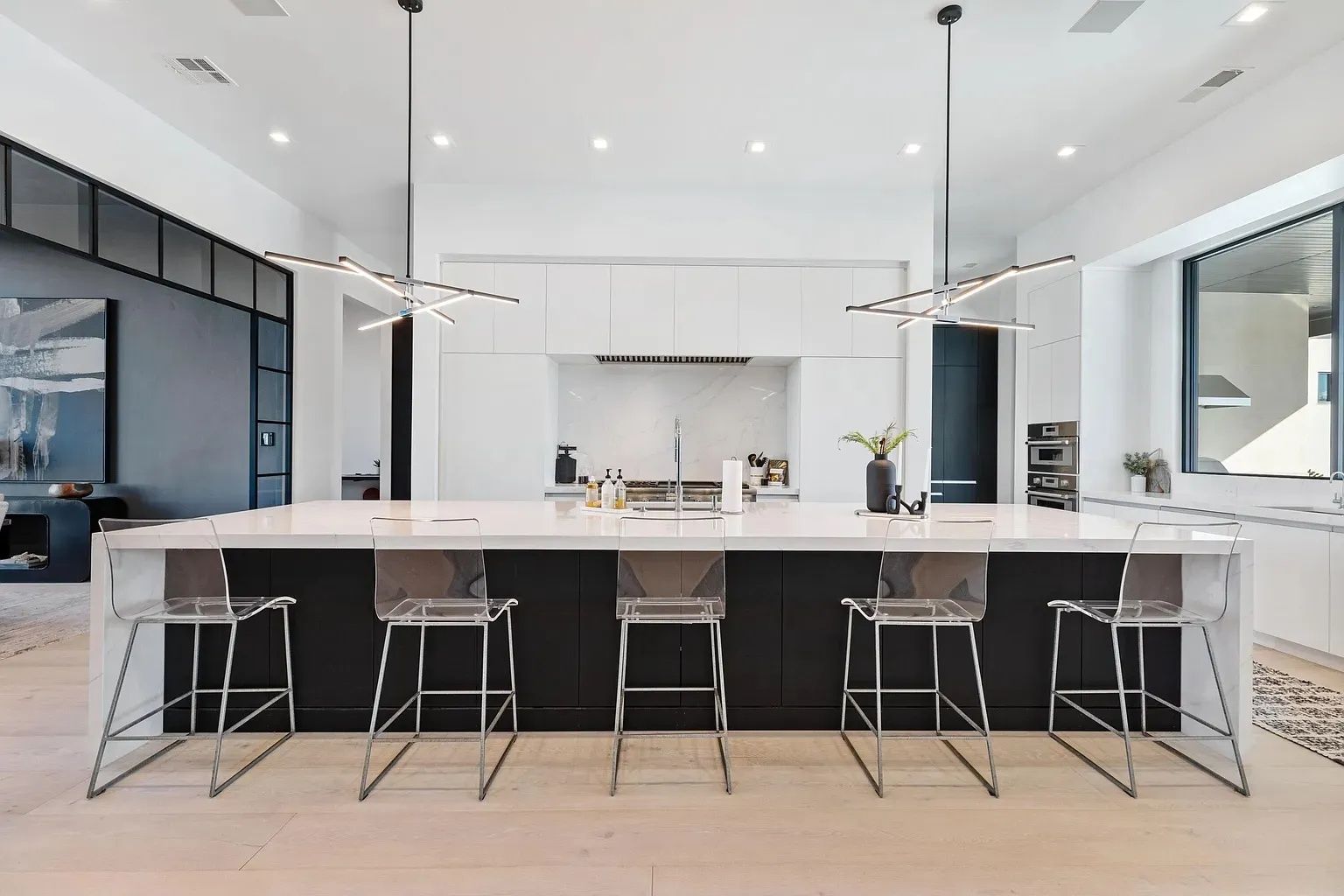 Modern kitchen with black and white cabinetry, large island with clear bar stools, and two pendant lights.