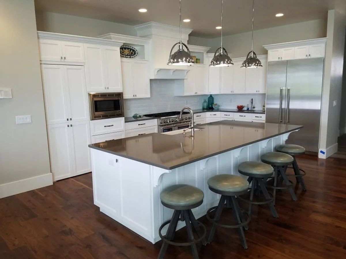 White kitchen with island, brown countertop, and industrial-style stools. Hardwood floors and stainless steel appliances.