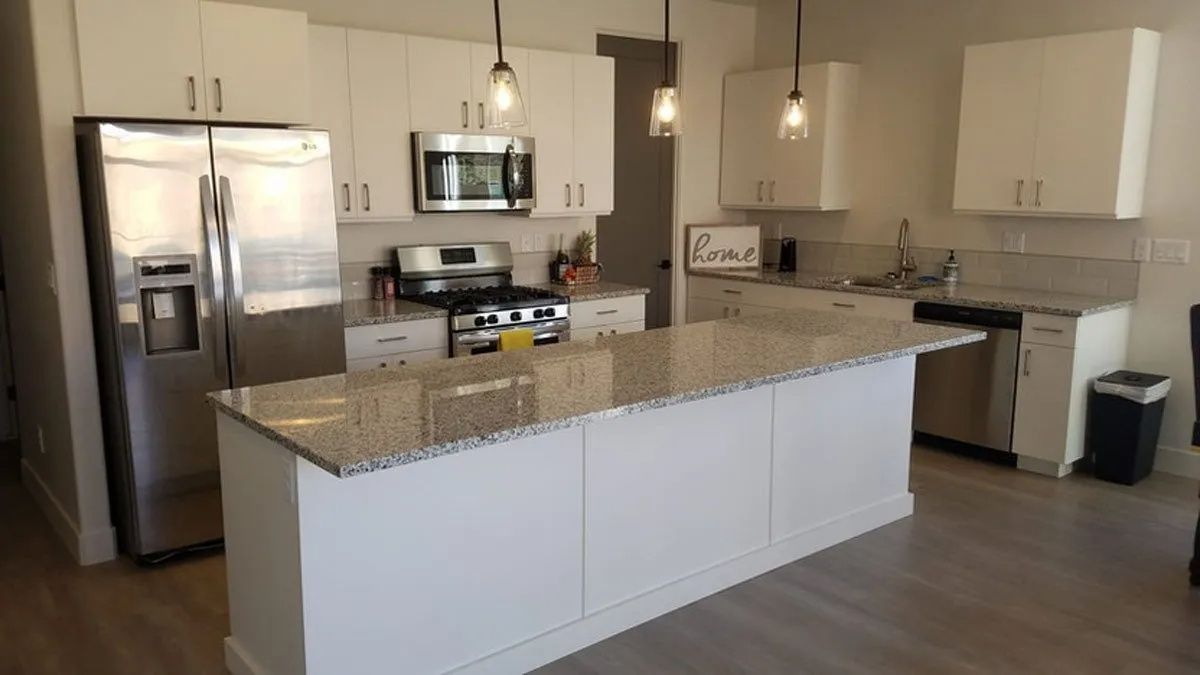 Modern kitchen with white cabinets, stainless steel appliances, and a granite island.