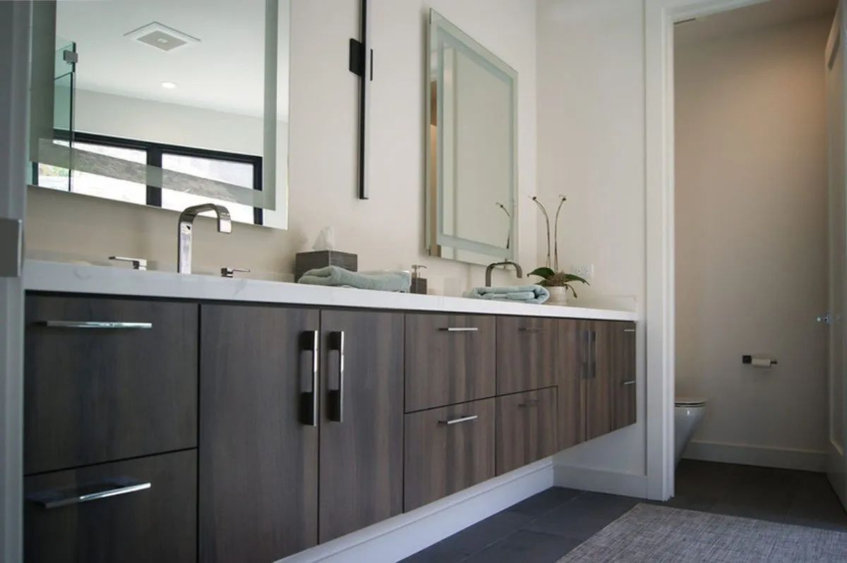 Modern bathroom with floating gray vanity, two mirrors, and a toilet visible in the doorway.