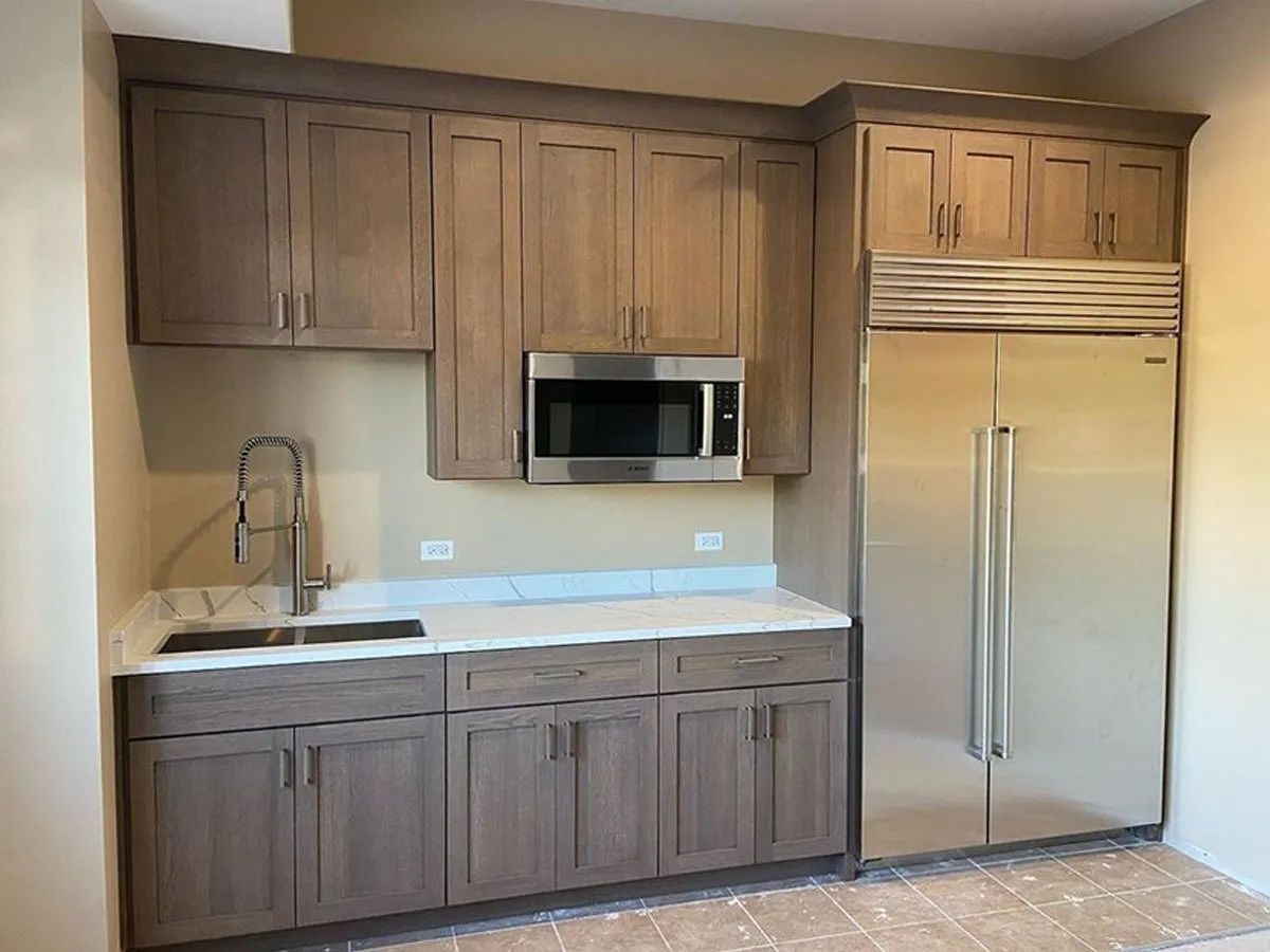 Small kitchen with wood cabinets, stainless steel refrigerator, microwave, sink, and white countertop.