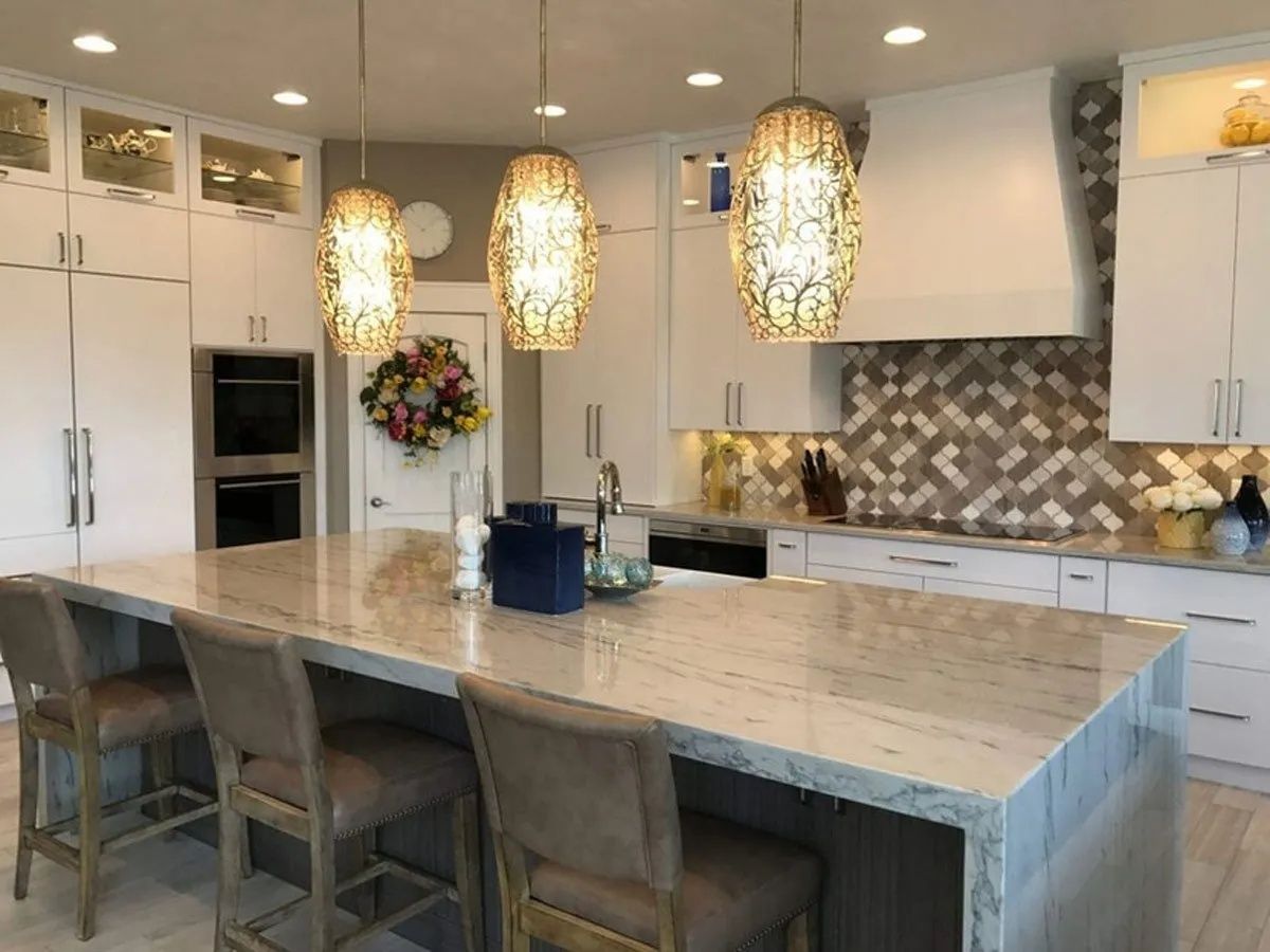 Modern kitchen with white cabinets, large island with bar stools, and three pendant lights.