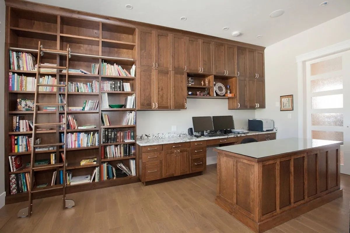 Wooden home office with built-in bookshelves, desk, and a ladder.