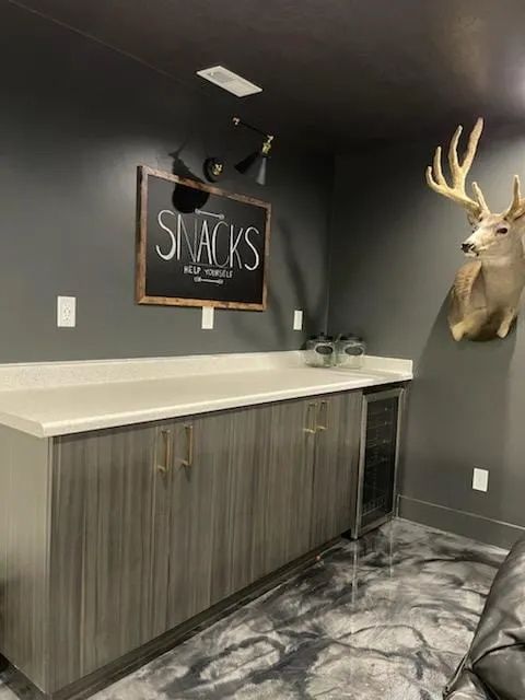 Dark gray snack bar with a deer head, chalkboard sign, and a built-in wine cooler.