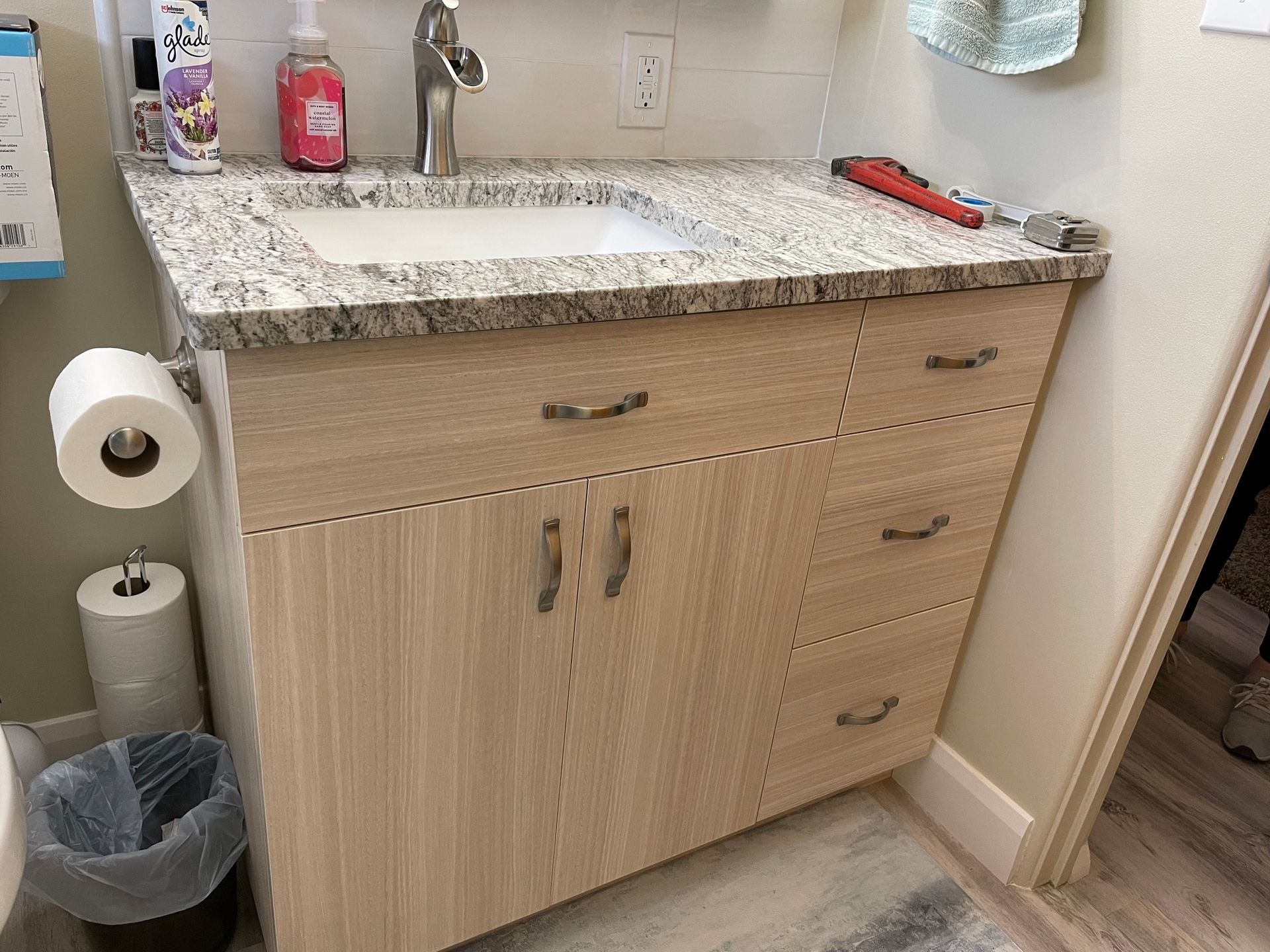 Bathroom vanity with light wood cabinets, granite countertop, and silver faucet.
