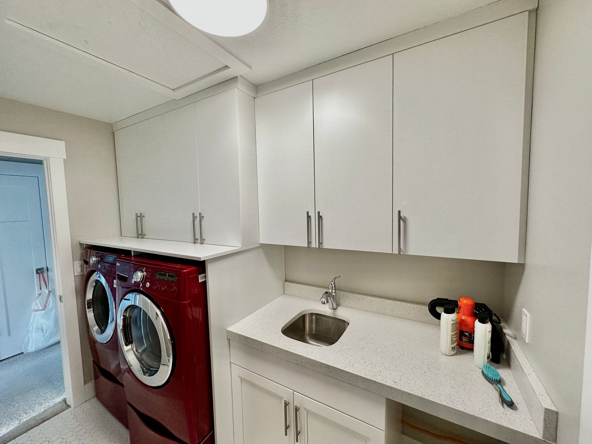 Red washer/dryer next to a utility sink and white cabinets in a laundry room.