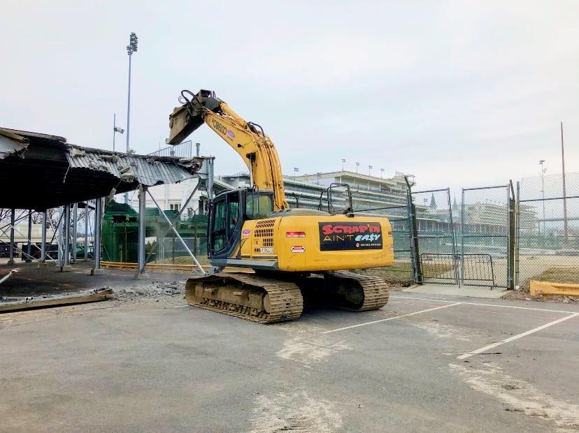 A yellow excavator is demolishing a building in a parking lot.
