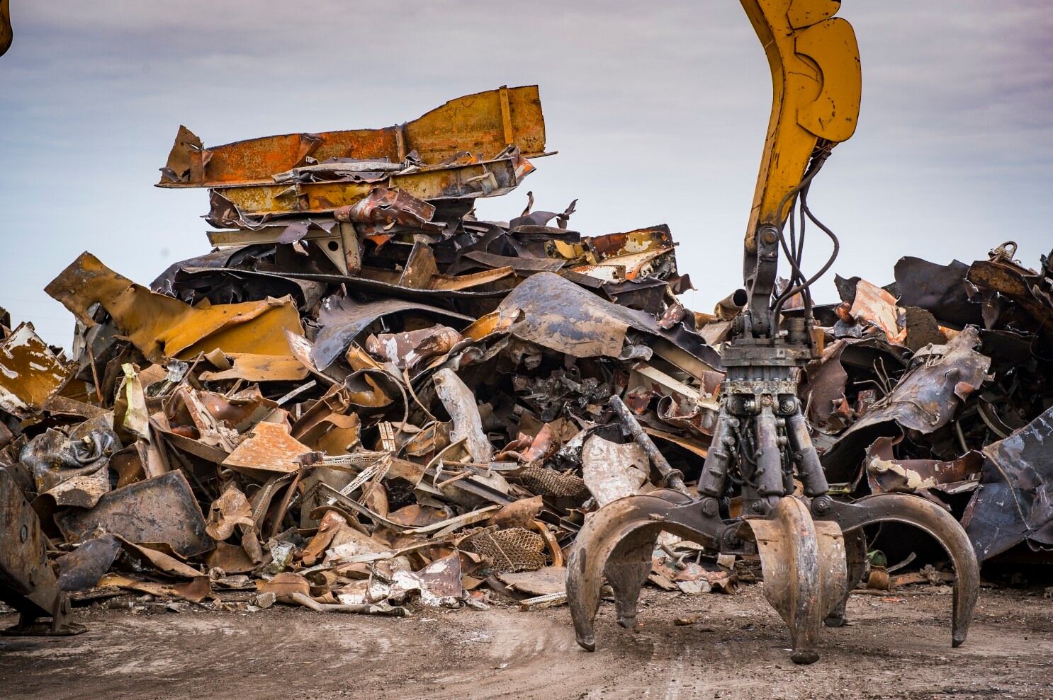 A yellow crane is reaching into a pile of scrap metal.